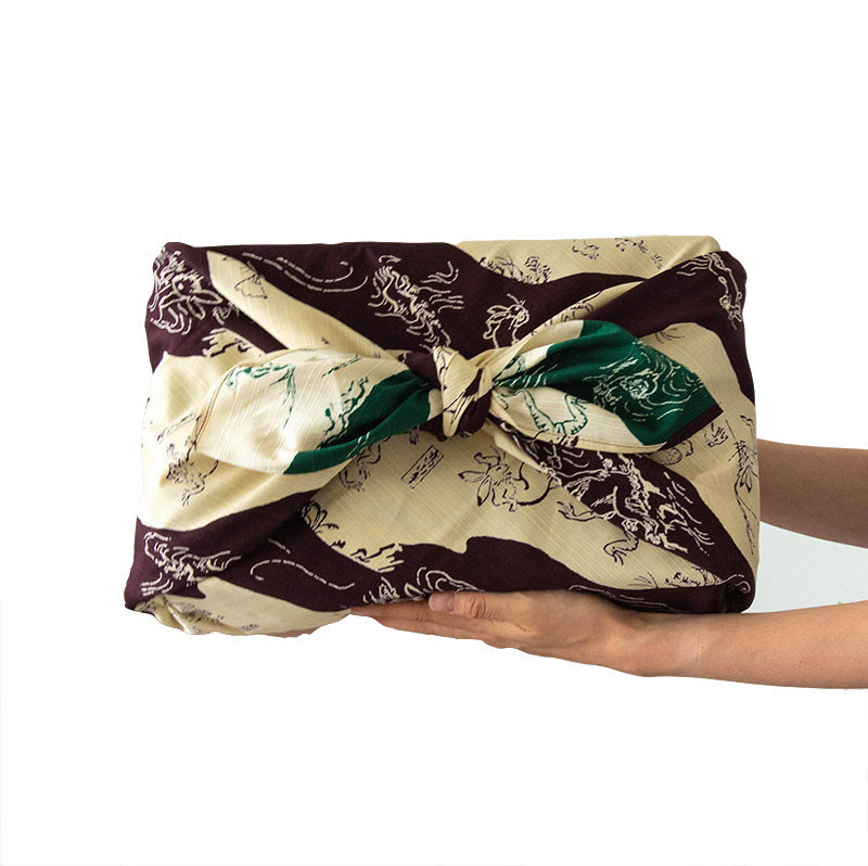 Hands holding package wrapped in a purple, green and ivory furoshiki